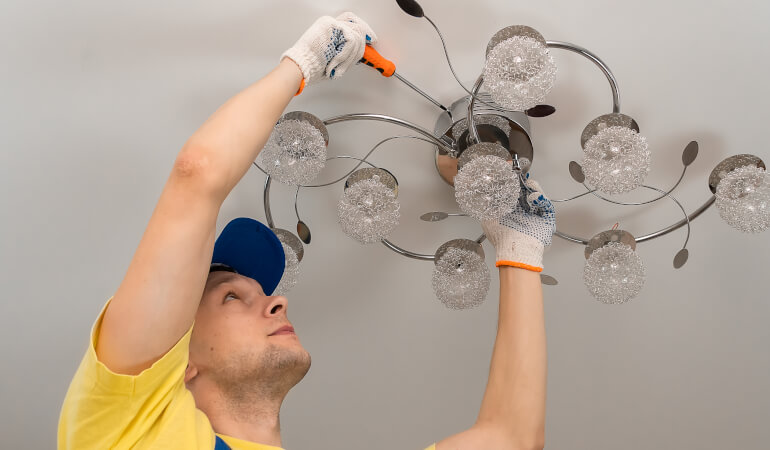 Electrician screws a chandelier to the ceiling close-up